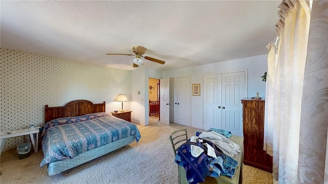 bedroom with a textured ceiling, two closets, light colored carpet, and ceiling fan