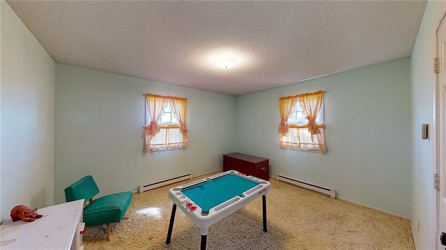 recreation room featuring a healthy amount of sunlight, a textured ceiling, and a baseboard heating unit