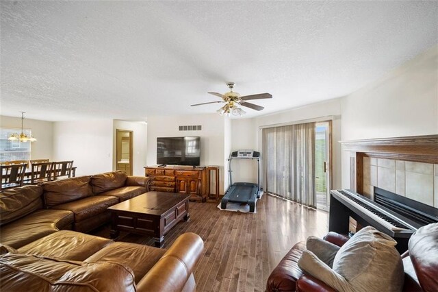 1116 N Mohican Ct, Independence, MO 64056 - living room featuring a textured ceiling, wood finished floors, a ceiling fan, a chandelier, and a tiled fireplace