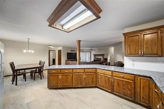 kitchen with kitchen peninsula, a textured ceiling, decorative columns, ceiling fan with notable chandelier, and decorative light fixtures