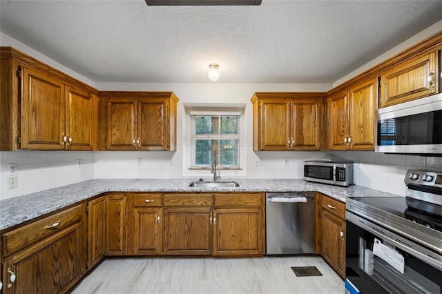 kitchen with decorative backsplash, a textured ceiling, light stone countertops, sink, and stainless steel appliances