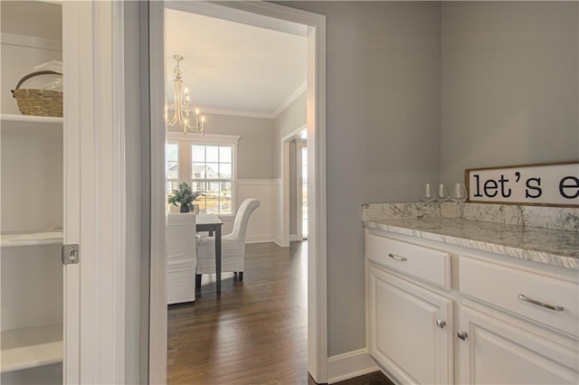 interior space featuring light stone countertops, white cabinetry, dark wood-type flooring, ornamental molding, and an inviting chandelier