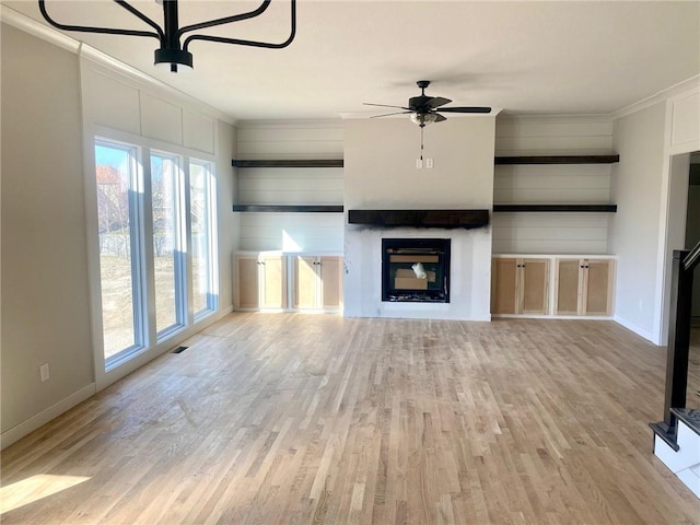 unfurnished living room featuring light wood finished floors, crown molding, baseboards, ceiling fan, and a glass covered fireplace