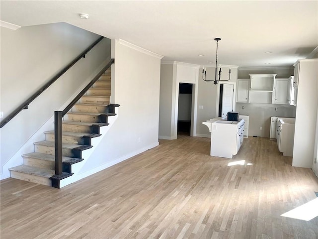 kitchen featuring baseboards, light wood-style flooring, pendant lighting, white cabinetry, and crown molding