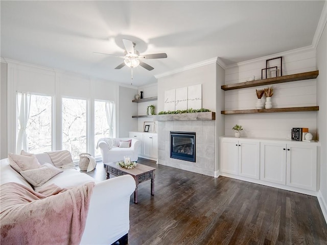 living room with a ceiling fan, dark wood-style flooring, crown molding, and a tiled fireplace