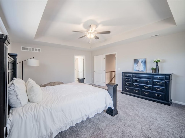 bedroom with a tray ceiling, carpet flooring, baseboards, and visible vents