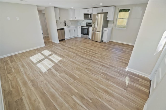 kitchen with backsplash, white cabinetry, sink, light hardwood / wood-style floors, and stainless steel appliances