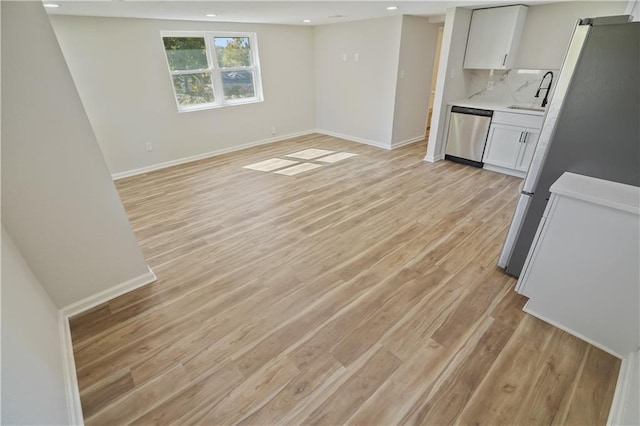 interior space with decorative backsplash, white cabinets, appliances with stainless steel finishes, light wood-type flooring, and sink