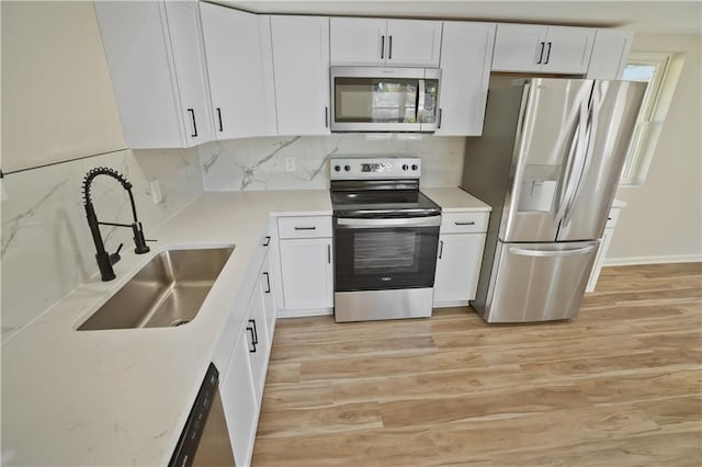 kitchen with appliances with stainless steel finishes, white cabinetry, sink, and light wood-type flooring