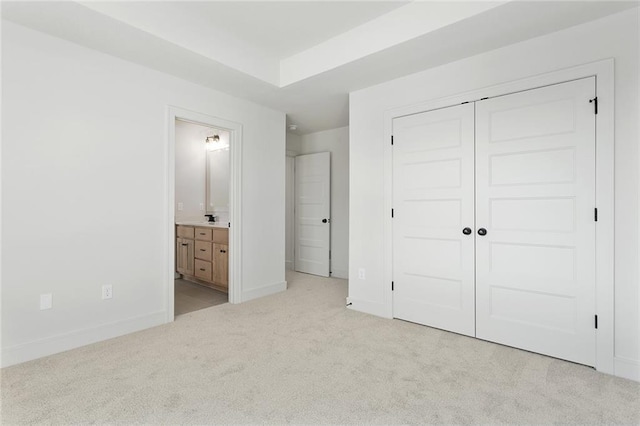 unfurnished bedroom featuring sink, connected bathroom, light colored carpet, and a closet