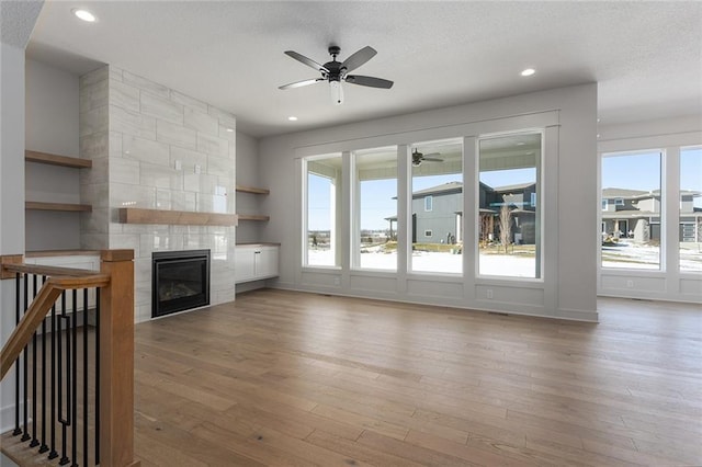 unfurnished living room featuring a tile fireplace, ceiling fan, and light hardwood / wood-style floors