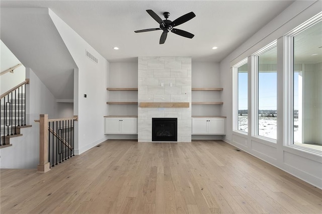 unfurnished living room featuring a tile fireplace, built in shelves, plenty of natural light, and light hardwood / wood-style flooring