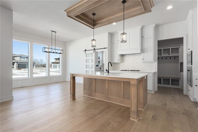 kitchen with white cabinetry, hanging light fixtures, a kitchen island with sink, a raised ceiling, and a barn door