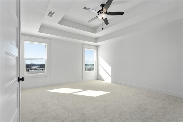 carpeted spare room with a raised ceiling and ceiling fan