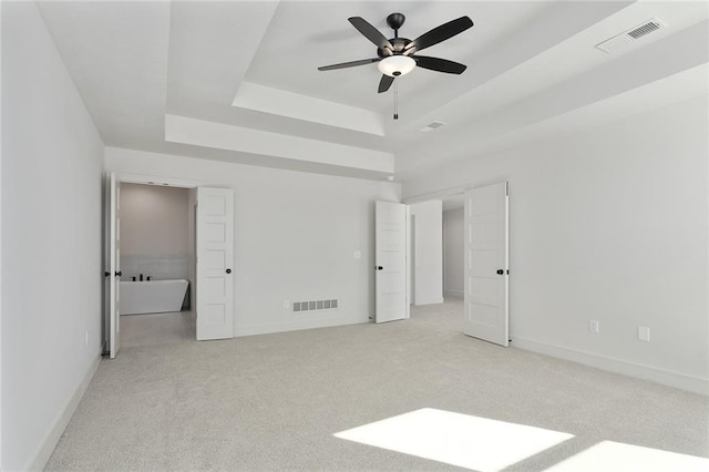 unfurnished bedroom with light carpet, ceiling fan, and a tray ceiling