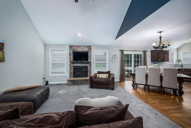 living room with a stone fireplace, vaulted ceiling, a notable chandelier, and light wood-type flooring