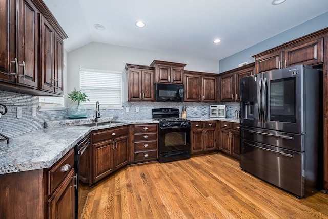 kitchen featuring tasteful backsplash, black appliances, sink, light wood-type flooring, and vaulted ceiling