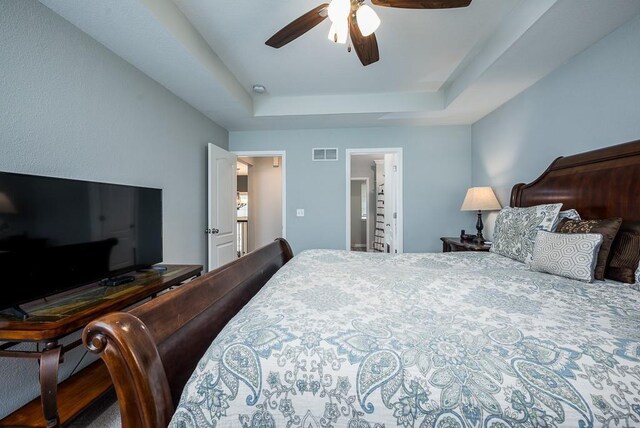 bedroom featuring connected bathroom, a tray ceiling, and ceiling fan