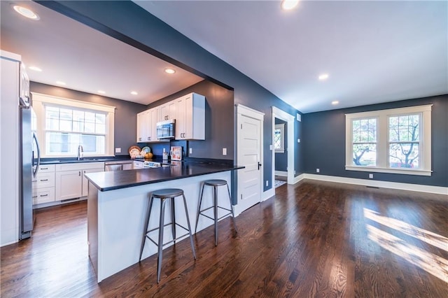 kitchen with appliances with stainless steel finishes, kitchen peninsula, a kitchen breakfast bar, white cabinets, and dark hardwood / wood-style floors