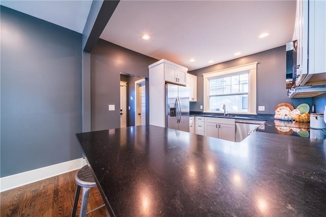 kitchen featuring sink, a kitchen bar, kitchen peninsula, white cabinetry, and stainless steel refrigerator with ice dispenser