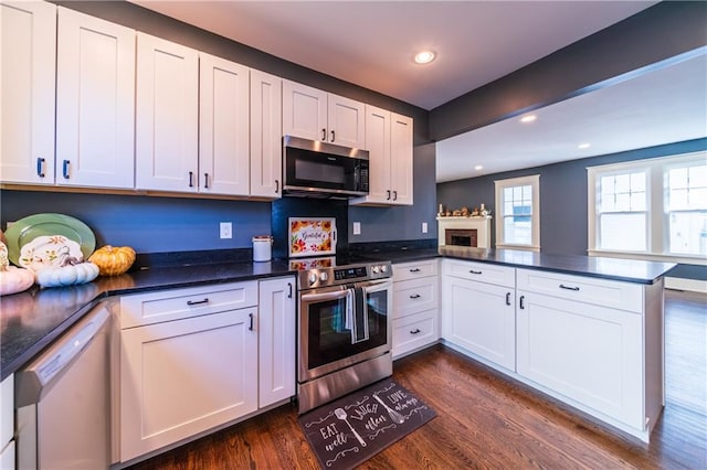 kitchen featuring appliances with stainless steel finishes, kitchen peninsula, white cabinetry, and dark wood-type flooring