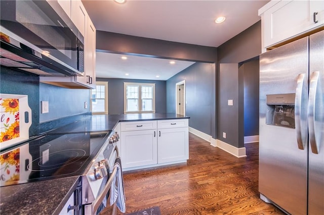 kitchen with kitchen peninsula, stainless steel appliances, dark stone countertops, white cabinetry, and dark hardwood / wood-style flooring