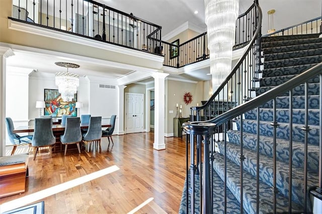 stairs featuring ornamental molding, hardwood / wood-style floors, ornate columns, and a towering ceiling