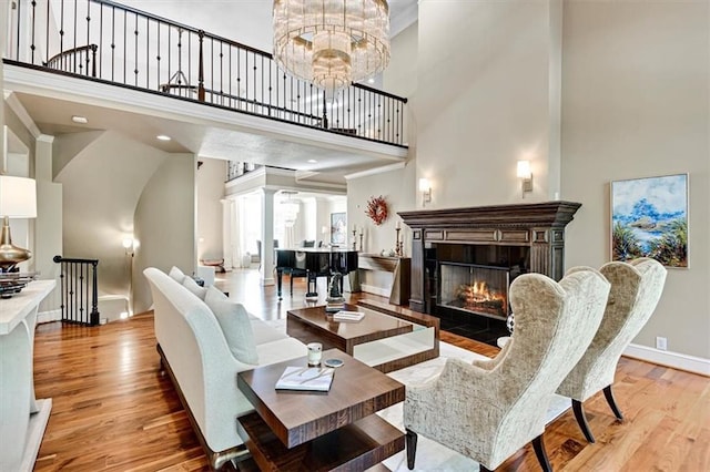 living room with ornate columns, a towering ceiling, an inviting chandelier, and light wood-type flooring