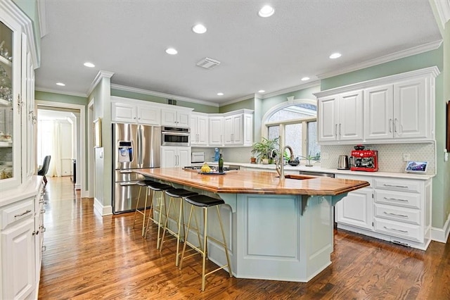 kitchen with butcher block countertops, appliances with stainless steel finishes, an island with sink, and white cabinets