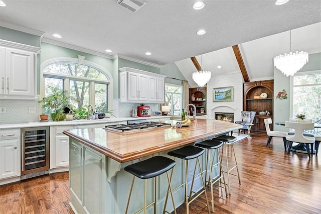 kitchen with a wealth of natural light, a kitchen island with sink, white cabinets, and beverage cooler