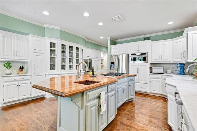 kitchen featuring white cabinets, appliances with stainless steel finishes, sink, an island with sink, and wooden counters