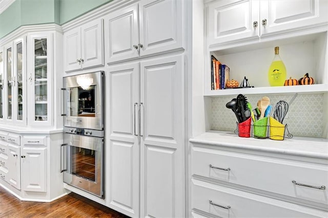 kitchen with dark wood-type flooring, tasteful backsplash, stainless steel double oven, and white cabinets