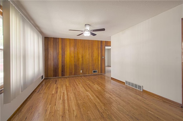 empty room featuring wooden walls, ceiling fan, and light wood-type flooring