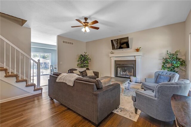 living room featuring dark wood-type flooring, a glass covered fireplace, visible vents, and stairway