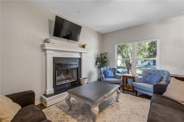 living area featuring baseboards, a tiled fireplace, and wood finished floors