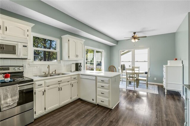 kitchen with a peninsula, white appliances, a sink, tasteful backsplash, and dark wood finished floors