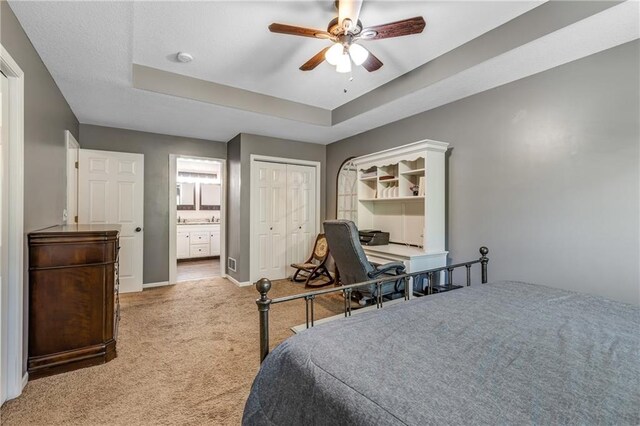 bedroom with a tray ceiling, a closet, light colored carpet, ceiling fan, and baseboards