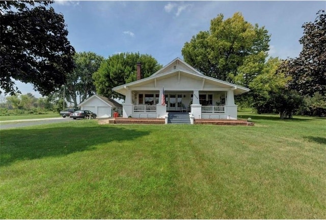 view of front of house with a front yard, a garage, an outbuilding, and a porch