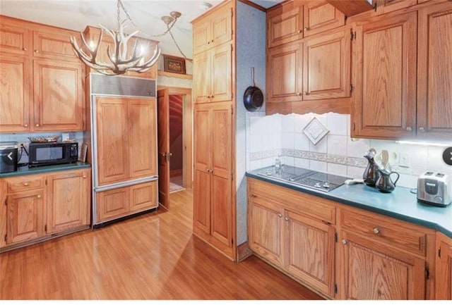 kitchen featuring backsplash, stainless steel stovetop, decorative light fixtures, light hardwood / wood-style flooring, and a chandelier