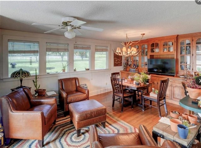 living room with ceiling fan with notable chandelier, a textured ceiling, and light hardwood / wood-style floors