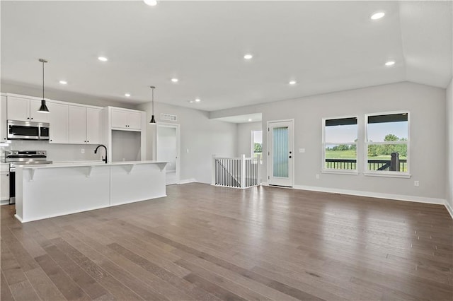 kitchen with white cabinets, a center island with sink, appliances with stainless steel finishes, dark wood-type flooring, and decorative light fixtures