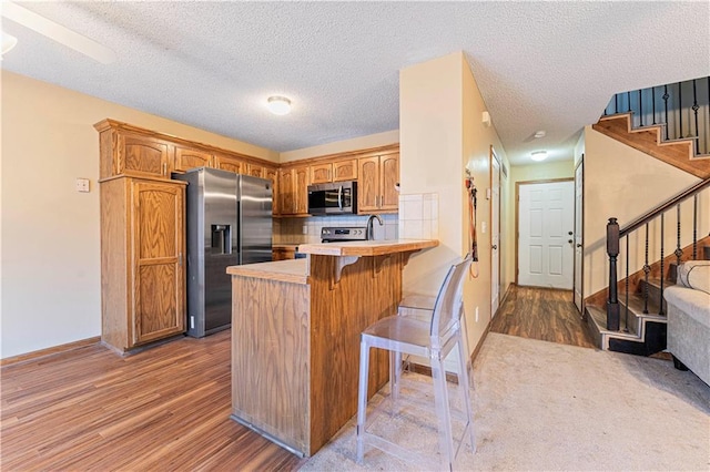 kitchen with stainless steel appliances, kitchen peninsula, a textured ceiling, and a breakfast bar