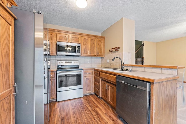 kitchen featuring stainless steel appliances, dark hardwood / wood-style floors, a textured ceiling, decorative backsplash, and kitchen peninsula