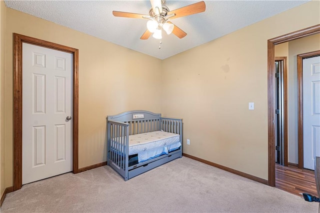 bedroom with a nursery area, light carpet, and ceiling fan