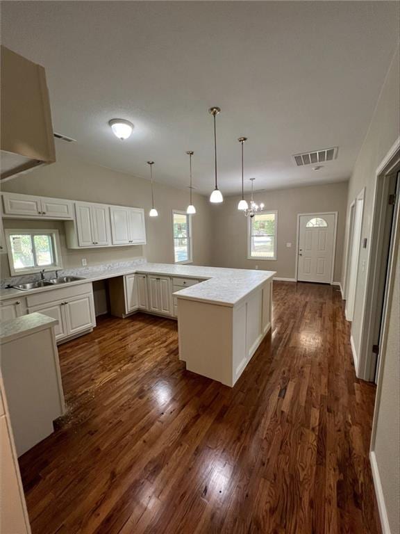 kitchen with sink, hanging light fixtures, white cabinets, dark wood-type flooring, and a notable chandelier