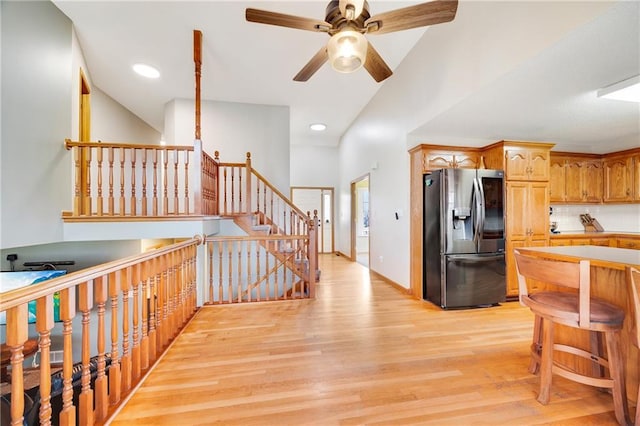 kitchen with stainless steel refrigerator with ice dispenser, light wood-type flooring, backsplash, ceiling fan, and high vaulted ceiling