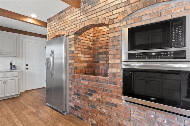 kitchen with appliances with stainless steel finishes, white cabinets, brick wall, and light hardwood / wood-style floors