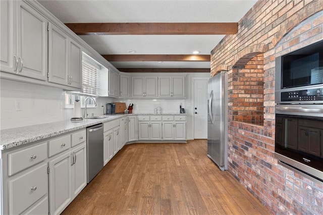 kitchen featuring appliances with stainless steel finishes, beam ceiling, sink, and light hardwood / wood-style floors