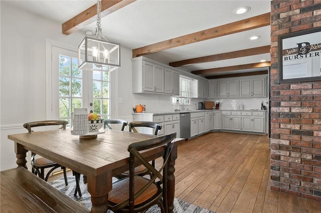 dining space featuring a notable chandelier, beam ceiling, sink, and wood-type flooring