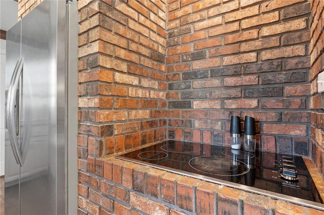 kitchen featuring brick wall, black electric stovetop, and stainless steel refrigerator with ice dispenser